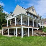 A spacious house with a large porch, multiple columns, and two stories overlooks a well-maintained lawn and garden with an American flag on display.