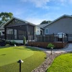 A backyard view featuring a covered patio with a screened-in area, a hot tub, a narrow stone path, and a small putting green surrounded by landscaping.